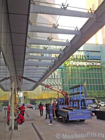 Монтаж большого стеклопакета манипулятором под козырьком здания в Москва-Сити.